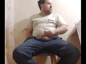 A chubby gay man sits down on a chair to pleasure himself.